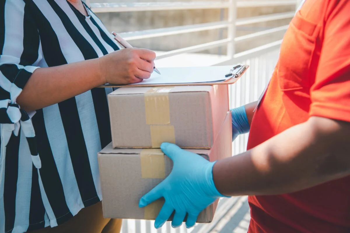 Consumismo, sus causas y consecuencias consumer is signing a document to receive a parcel from a home courier.